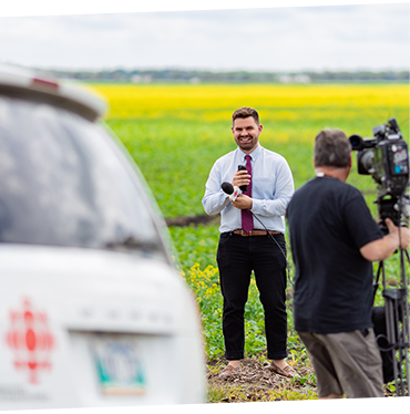 A journalist is getting ready to do a live on-site report. He stands in a canola field.